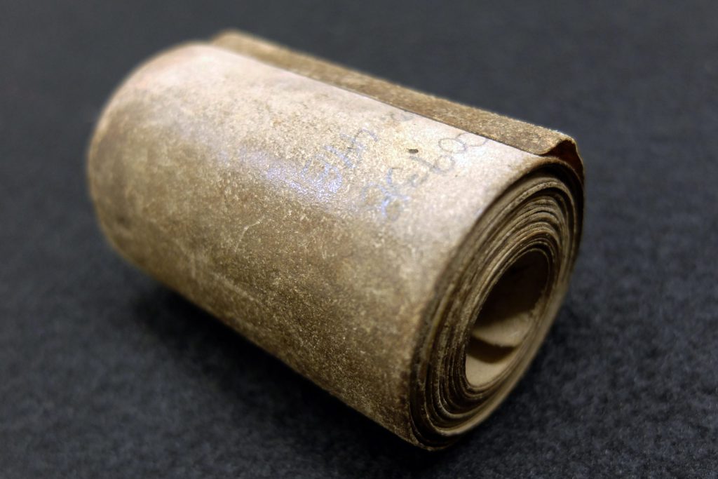Das Bild zeigt Amulett aus dem 17. Jh., welches aussieht wie eine fein säuberlich zusammengerollte Schriftrolle.
