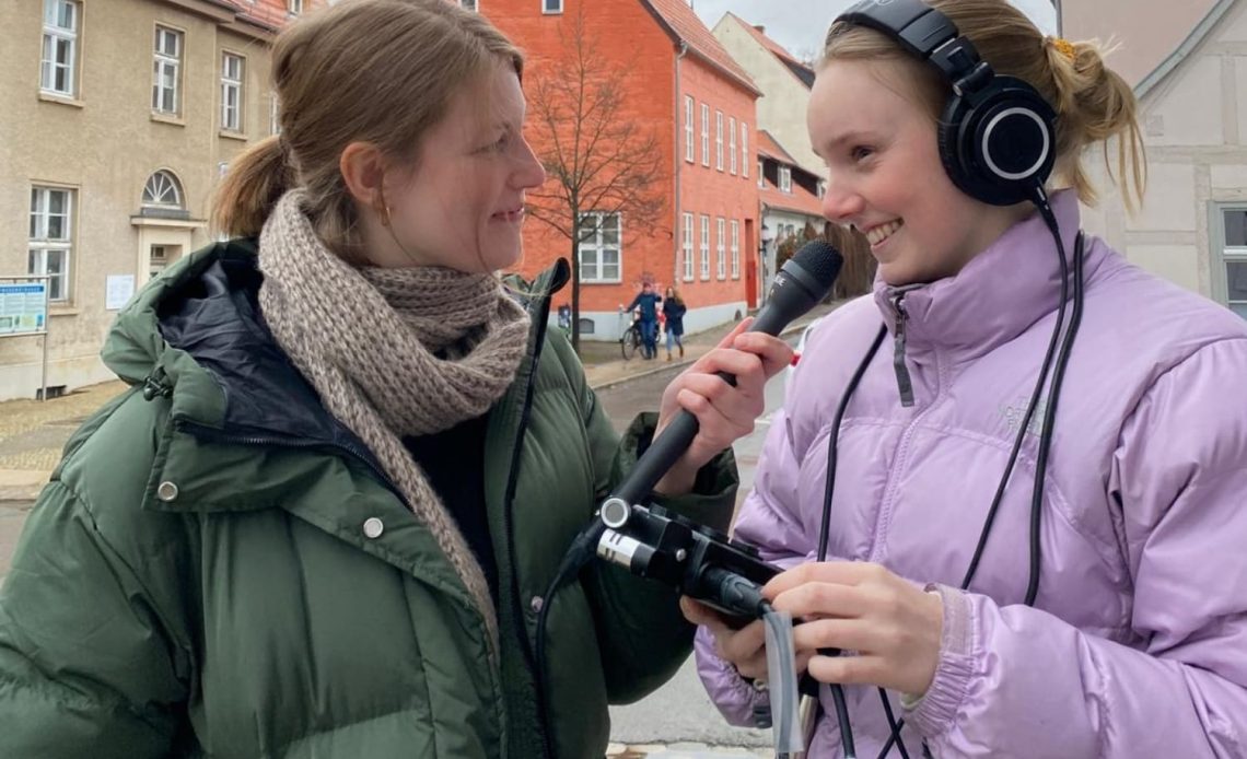 Zwei junge Studentinnen stehen auf der Straße und interviewen sich mit einem Aufnahmegerät und einem Mikrofon.