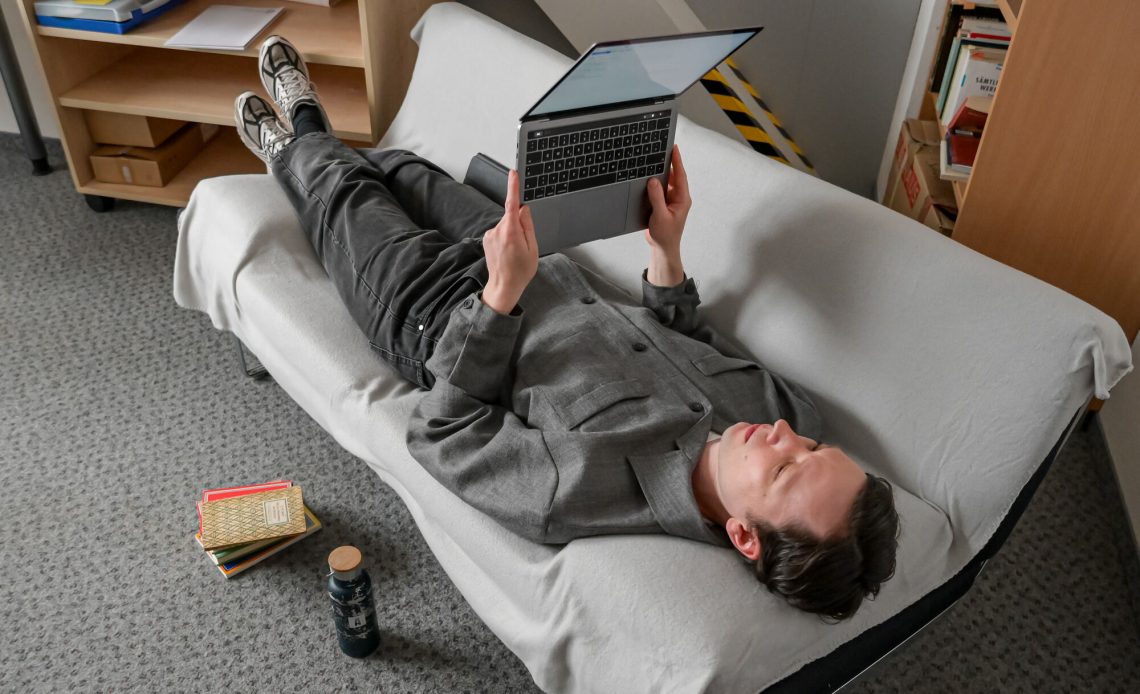 Portrait Dr. Elias Kreuzmair. Er liegt auf einem Sofa und liest auf dem Laptop