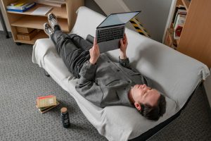 Portrait Dr. Elias Kreuzmair. Er liegt auf einem Sofa und liest auf dem Laptop