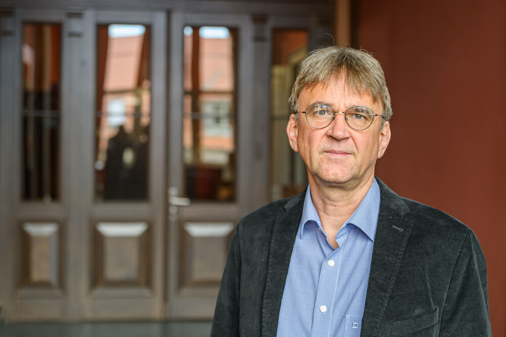 Auf dem Portrait ist Prof. Dr. Wolfgang Kesselheim zu sehen. Er hat kurze braune Haare, trägt eine runde Brille und lächelt freundlich in die Kamera