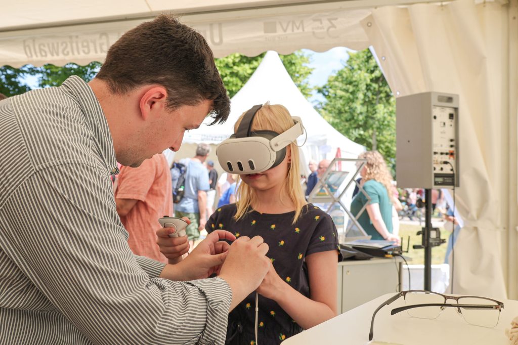Ein Wissenschaftler erklärt einem Mädchen die Anwendung einer VR-Brille.