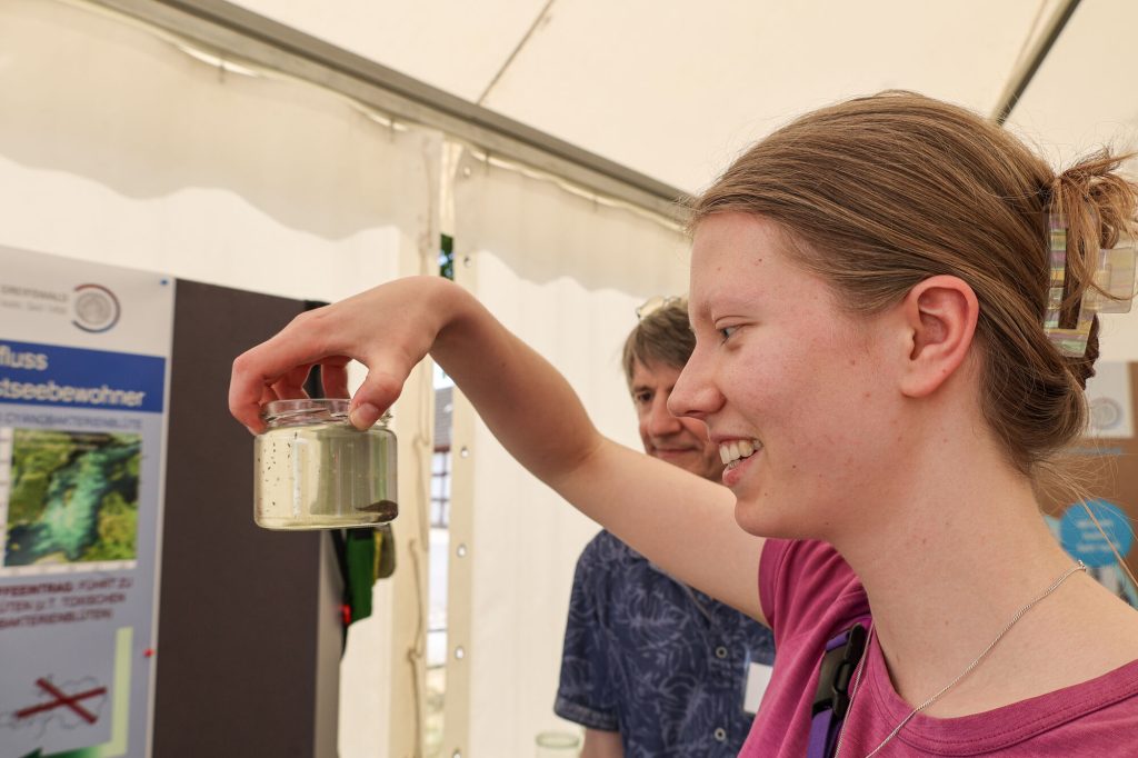 Eine Wissenschaftlerin betrachtet ein Glas, in dem ein Urzeitkrebs schwimmt.