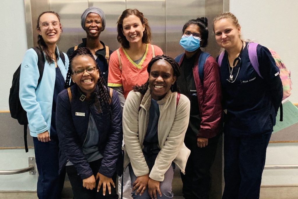 Das Foto zeigt viele lächelnde Frauen, die teilweise noch in Arbeitskleidung vor einem Fahrstuhl in einem Krankenhaus posieren.