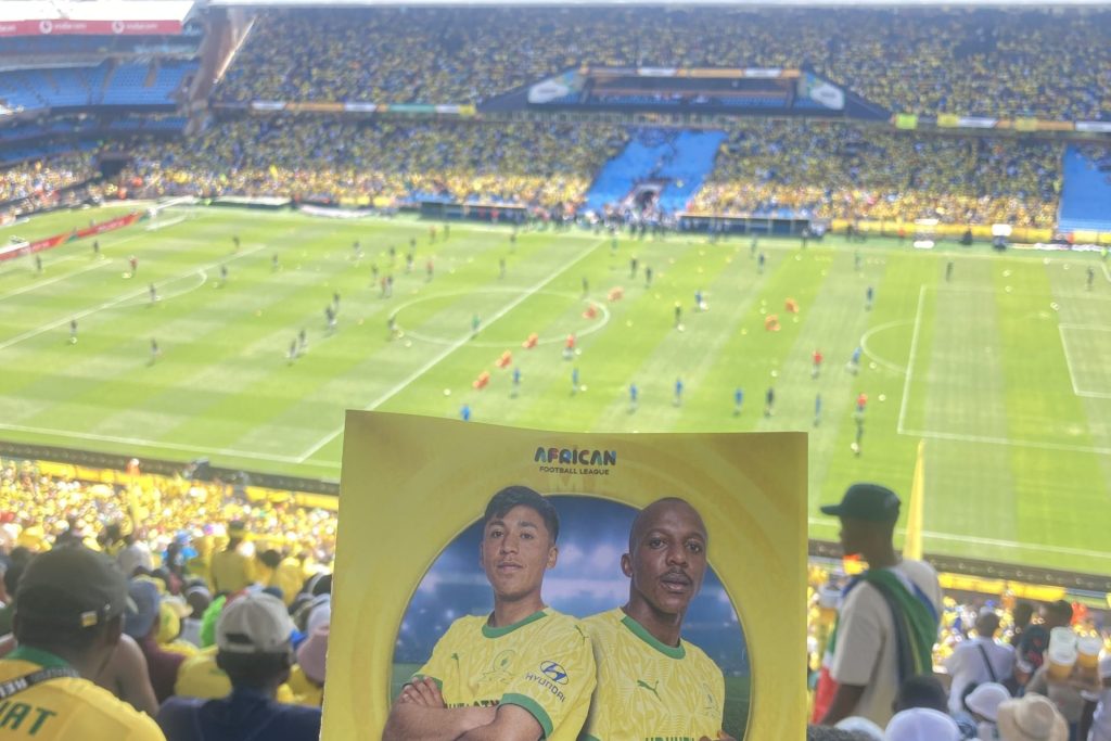 Das Foto zeigt ein Stadion, in dem Fußball gespielt wird. Das Stadion ist groß und die Ränge sind voll besetzt.