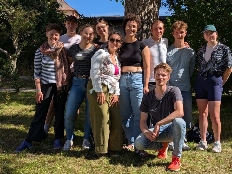 Das Foto zeigt eine Gruppe Studierender, die vor einem Baum stehen und nett in die Kamera lächeln.
