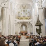 Im Dom St. Nikolai sitzen zahlreiche Menschen auf den Bänken der Kirche und