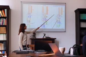 The photo shows Mariia defending her Master theses. She stands in front of a canvas and describes images that can be seen on this canvas.