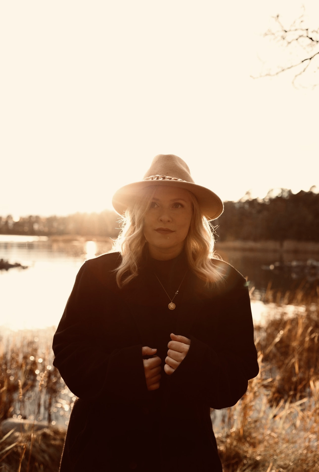 Eine Frau mit blonden Haaren und Hut steht im Herbst vor einem See