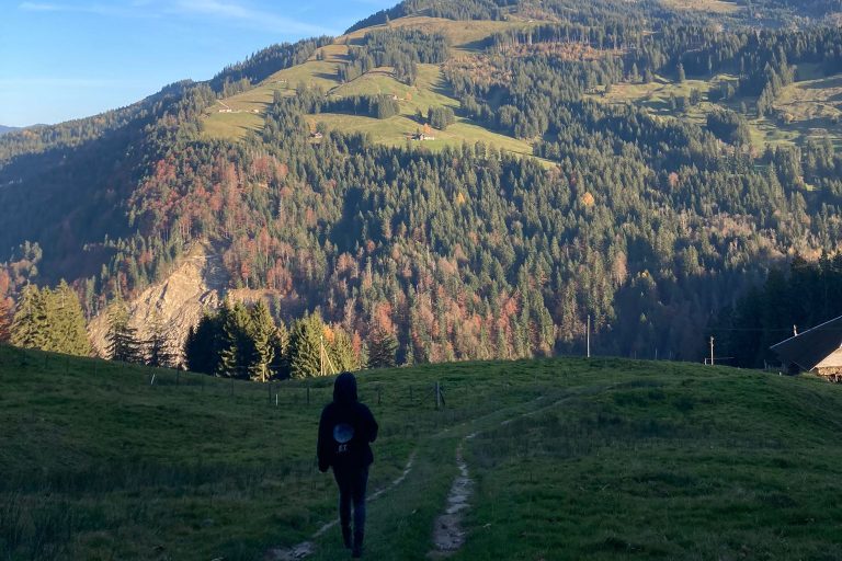 Auf dem Foto ist Jeanne D’Arc in den Bergen zu sehen. Sie steht mit dem Rücken zur Kamera und schaut auf die Natur.