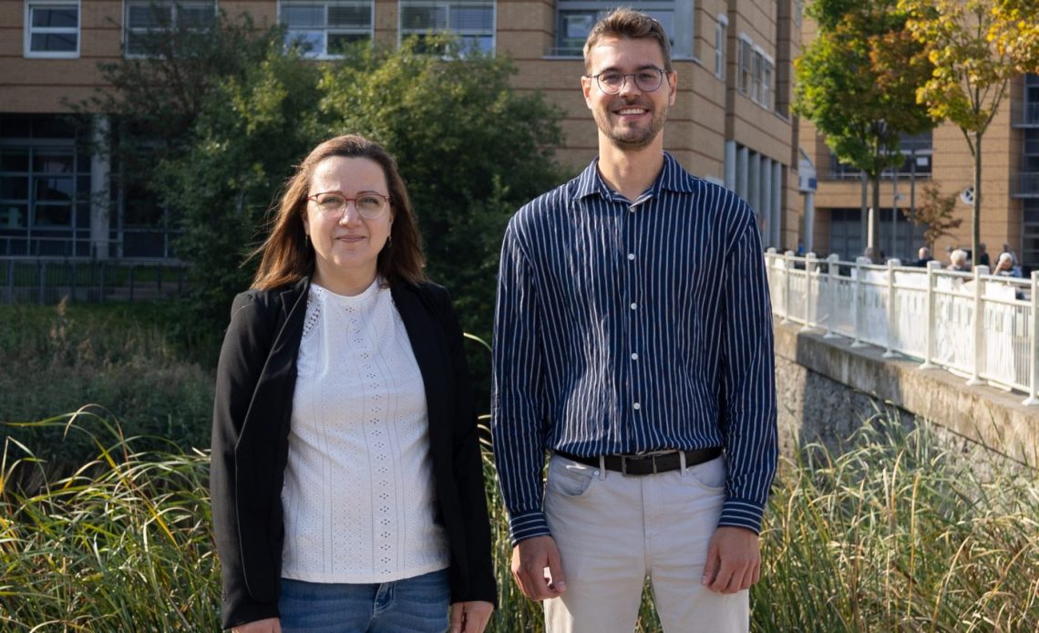 Zwei Forschende stehen vor der Universitätsmedizin und lächeln.