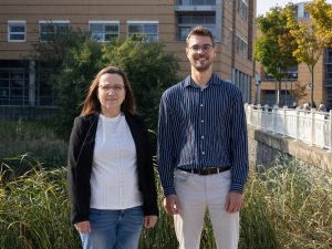 Zwei Forschende stehen vor der Universitätsmedizin und lächeln.