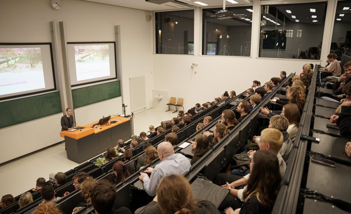 Viele Studierende sitzen in einem Hörsaal und hören dem studentischen Prorektor bei einer Rede zum Semesterempfang zu.