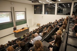 Viele Studierende sitzen in einem Hörsaal und hören dem studentischen Prorektor bei einer Rede zum Semesterempfang zu.
