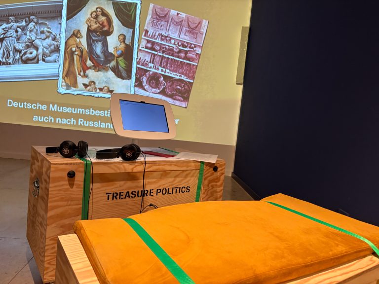 Ein Film läuft an einer Wand zum Thema Wikingergold, davor steht eine Bank und eine Holztruhe