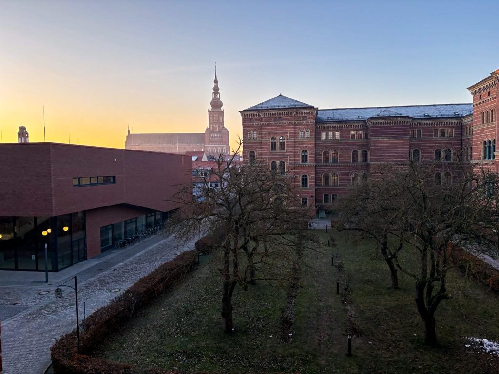 Blick auf einem Fenster auf einen Obstgarten, alte Unigebäude und den Dom St. Nikolai