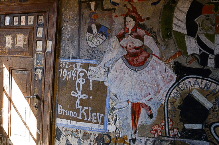 Das Foto zeigt eine farbige Zeichnung an der Wand des Karzers. Es ist eine Frau, die als eine Art Ballerina dargestellt wird. Sie trägt ein rot-rosa-farbiges Kleid mit einem ausladenden weißen Rock, einer roten Strumpfhose und dunklen Ballerinas.