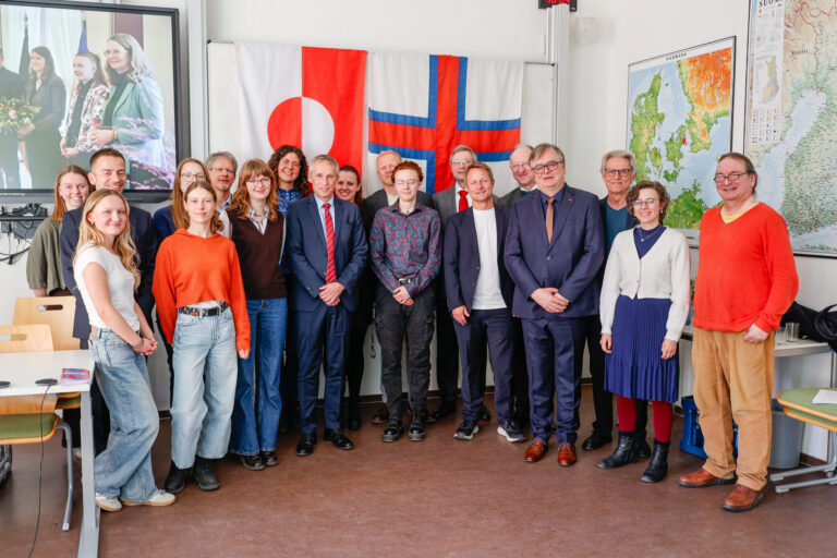 Auf dem Foto sind viele festlich gekleidete Menschen zu sehen. Sie stehen wie auf einem Gruppenfoto üblich nebeneinander in zwei Reihen und lächeln freundlich in die Kamera.