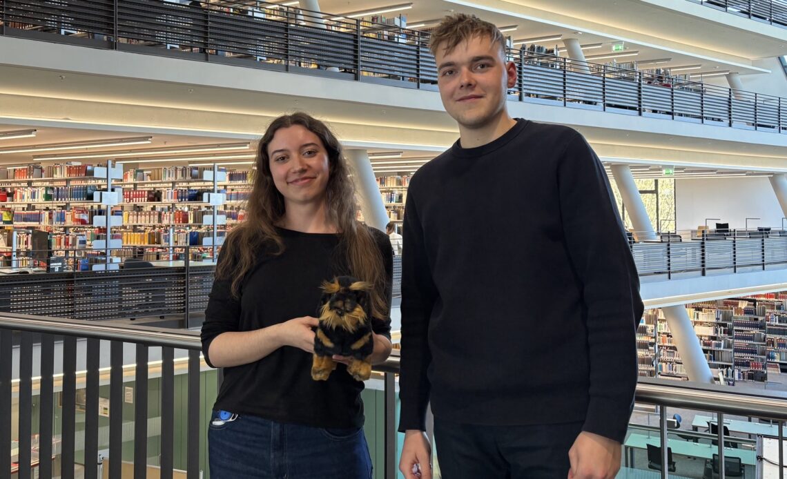 Eine junge Frau und ein junger Mann stehen in einer Bibliothek.
