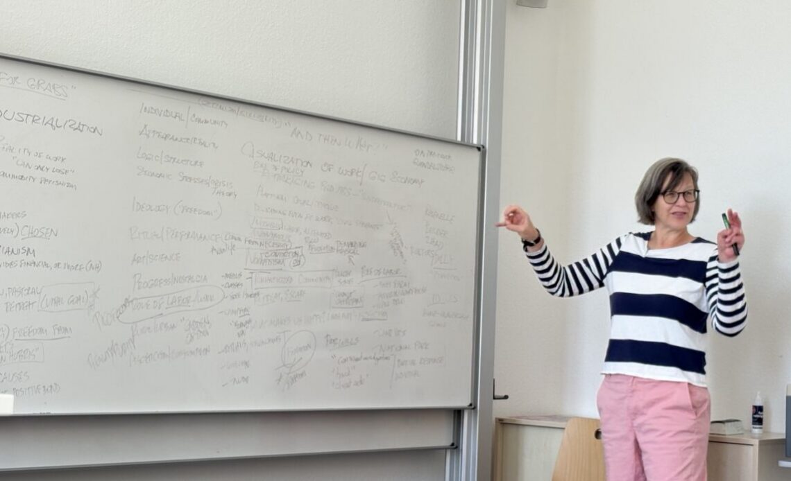 Eine Professorin erklärt an einer weißen Tafel den Seminarinhalt, während sie gestikuliert