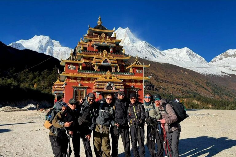 Es ist ein Tempel am Fuße von einem Berg zu sehen. Davor steht eine Gruppe Wanderer*innen, die breit lächelnd für ein Gruppenfoto posieren.