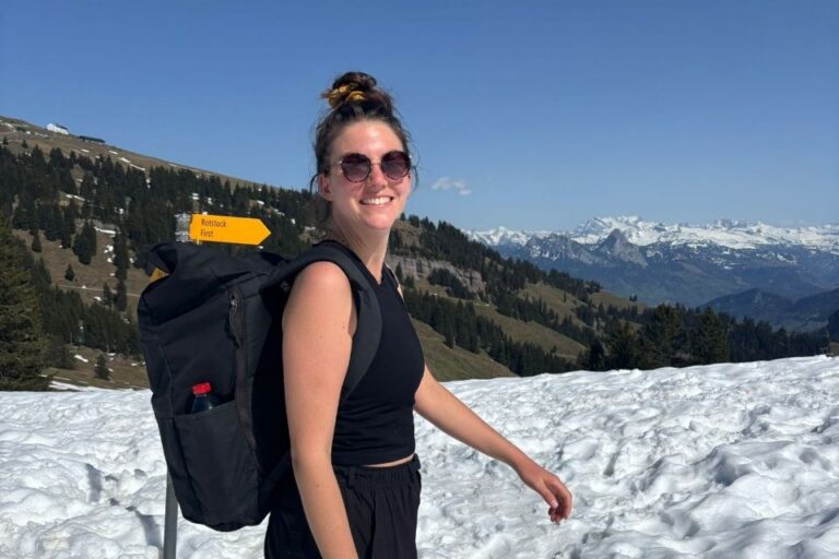 Das Foto zeigt eine junge Frau, wie sie im T-Shirt durch den Schnee läuft. Im Hintergrund sind ein blauer Himmel und Berge zu sehen.
