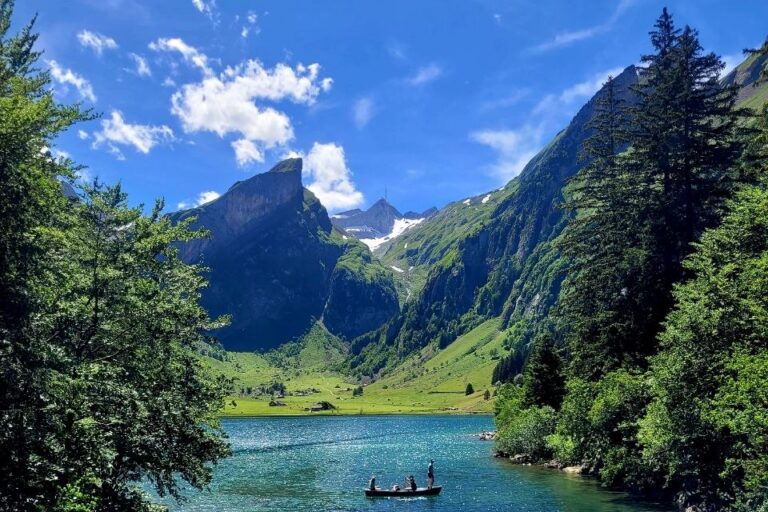 Das Foto zeigt einen klaren, blauen See am Fuße eines Berges. Auf dem See ist ein kleines Boot und der Himmel ist strahlend blau.
