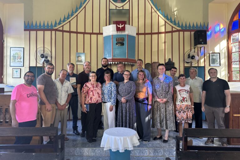 Es ist ein Gruppenfoto in einer Kirche zu sehen. Eine Gruppe von Menschen steht hinter dem Altar einer Kirche und lächelt freundlich in die Kamera.