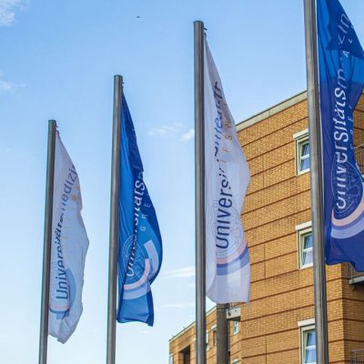 Vier gehisste Flaggen im Vordergrund der Universitätsmedizin Greifswald
